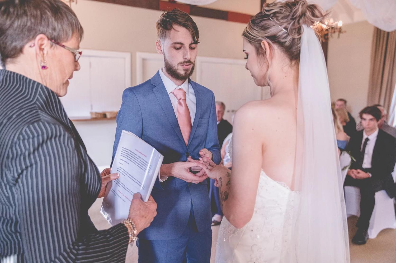 Celebrant reading the vows as the groom places the ring on the bride’s finger