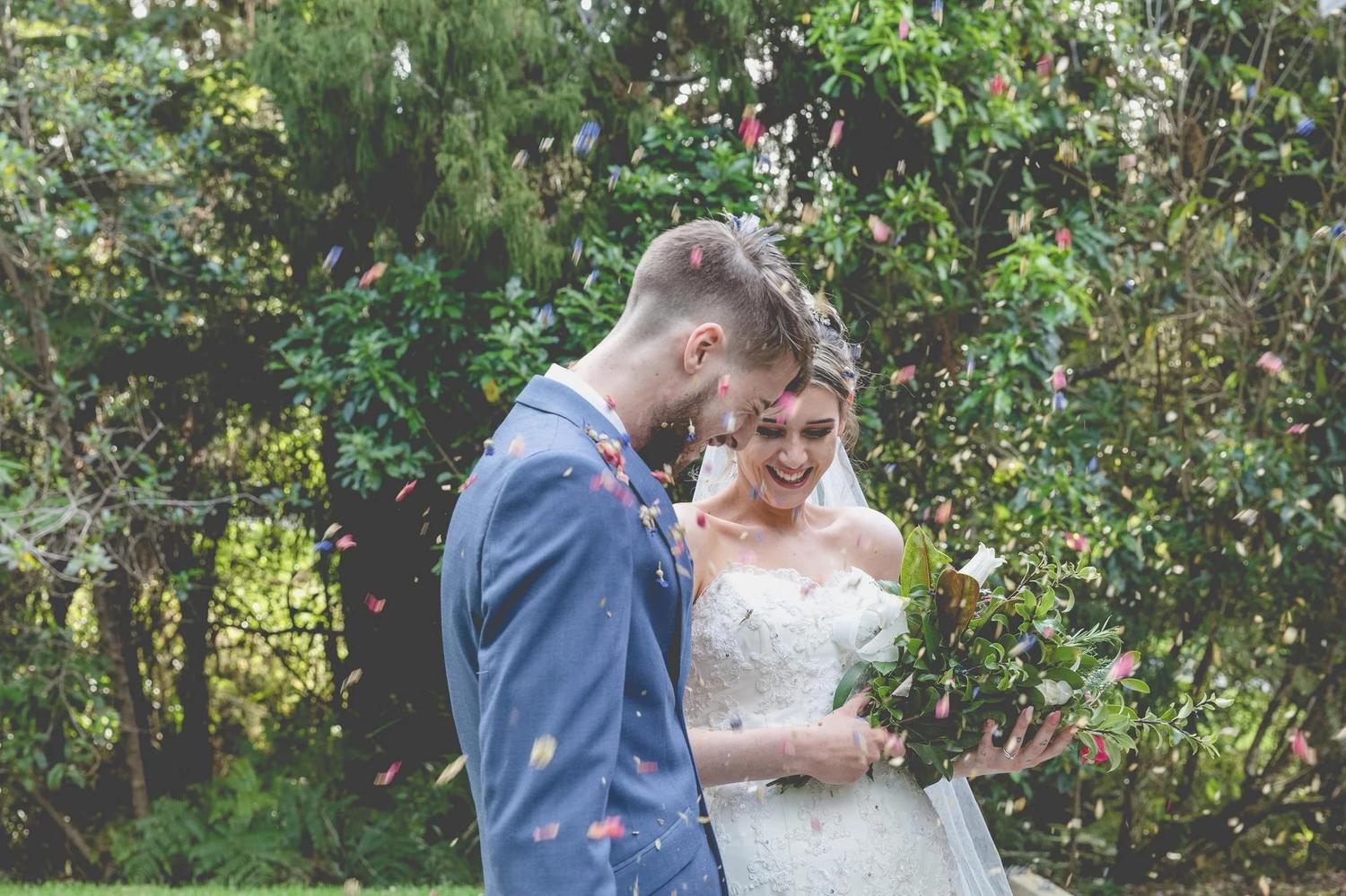 Bride and groom laughing as coloured confetti falls around them