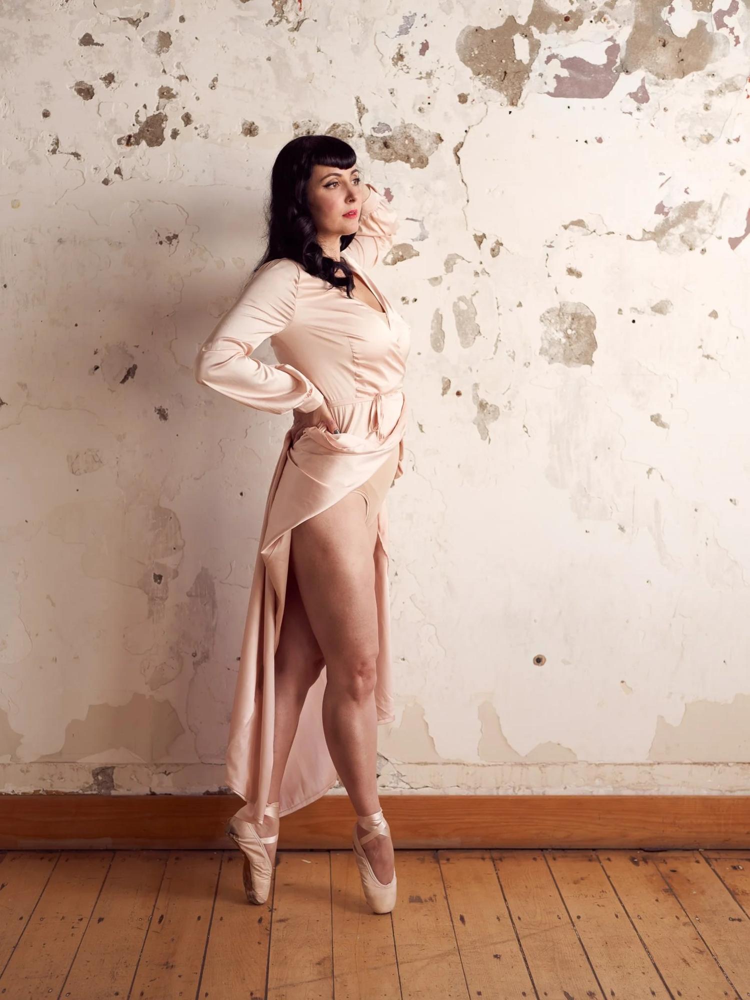 Viv stands on pointe against a peeling plaster wall