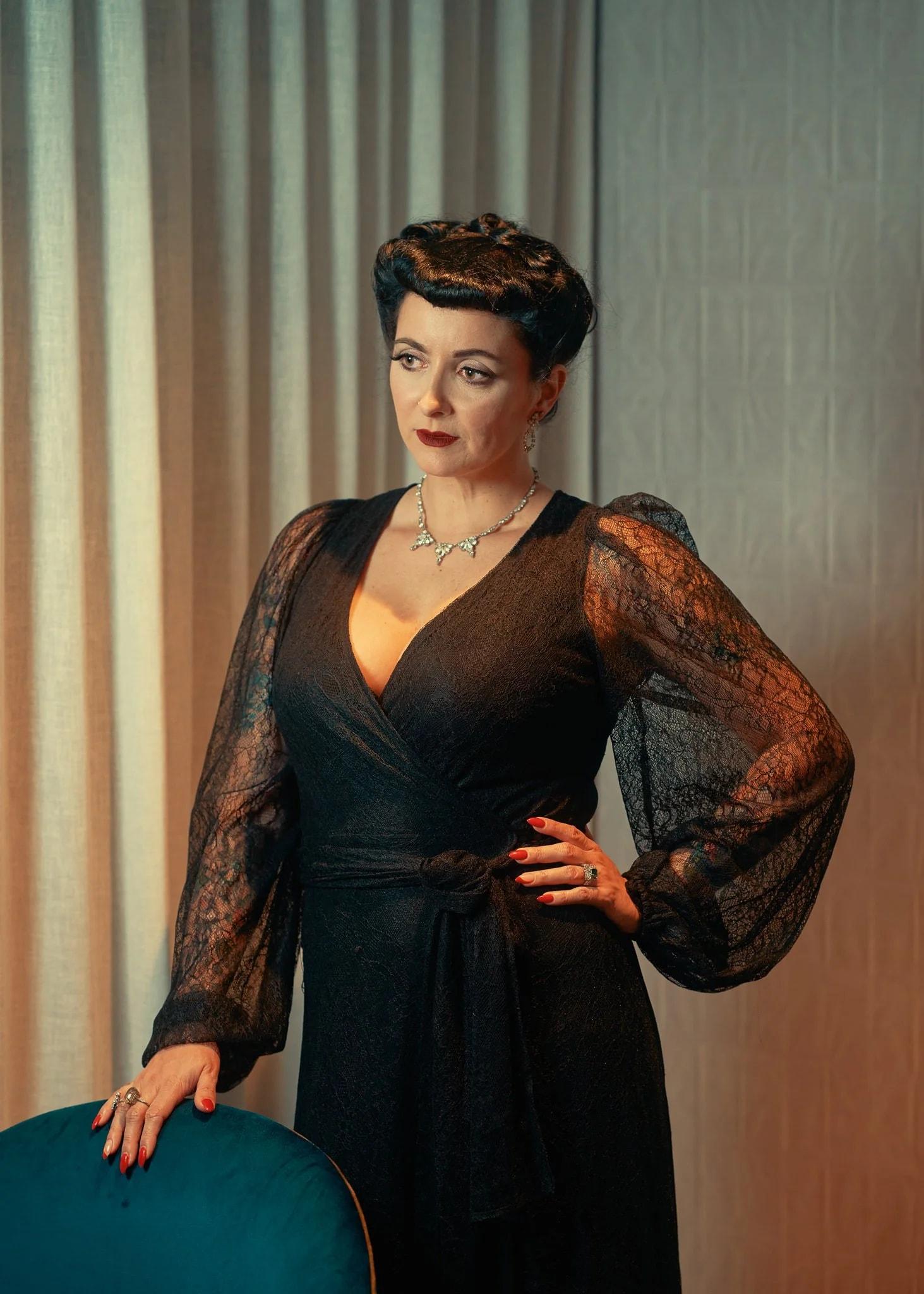 Viv in a black lace gown with a hand on her hip