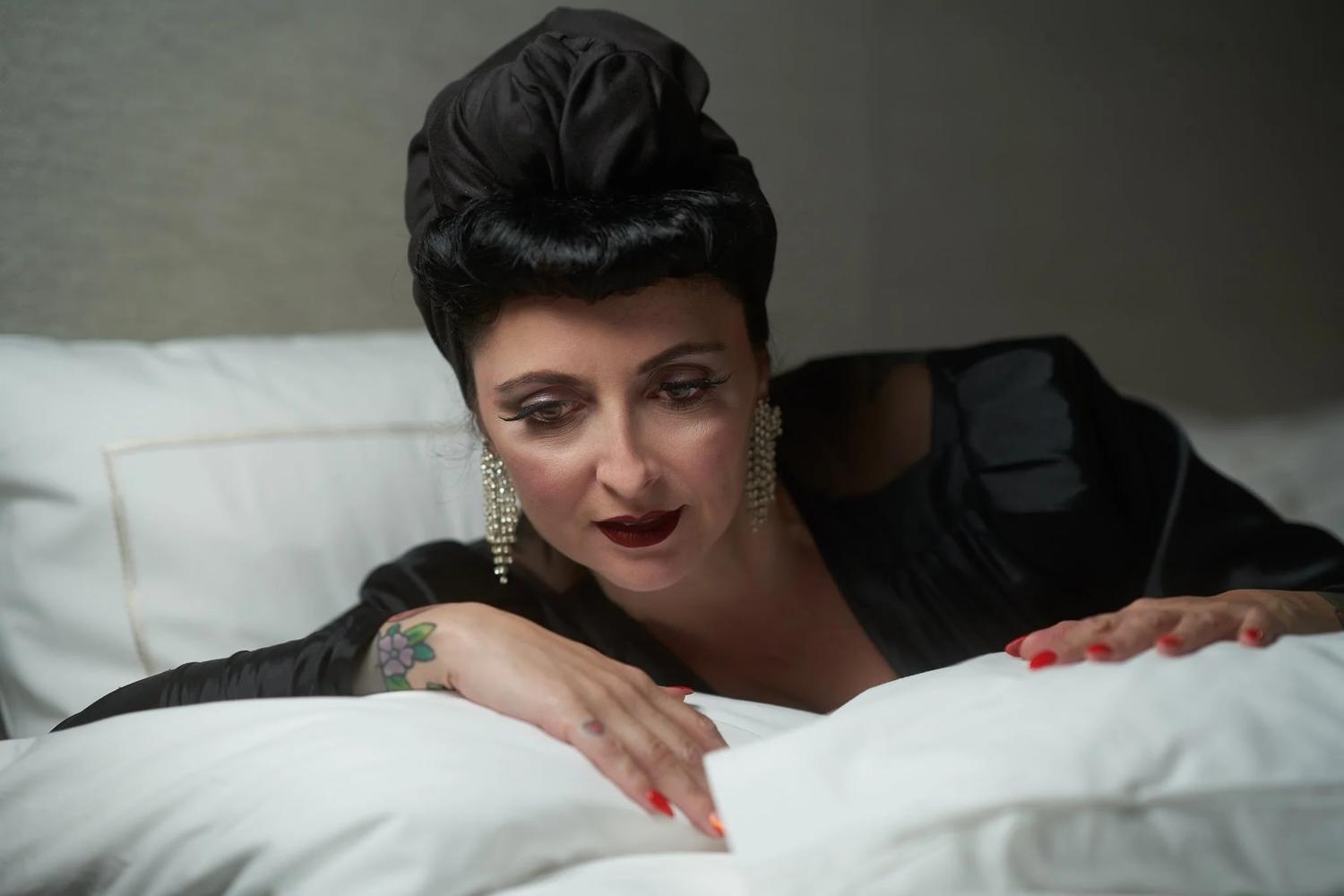 Viv leans on white pillows with red lips