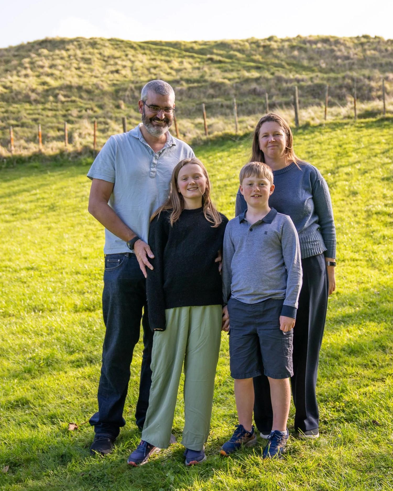 A family of four stands together on a grassy hill at Cornwall Park
