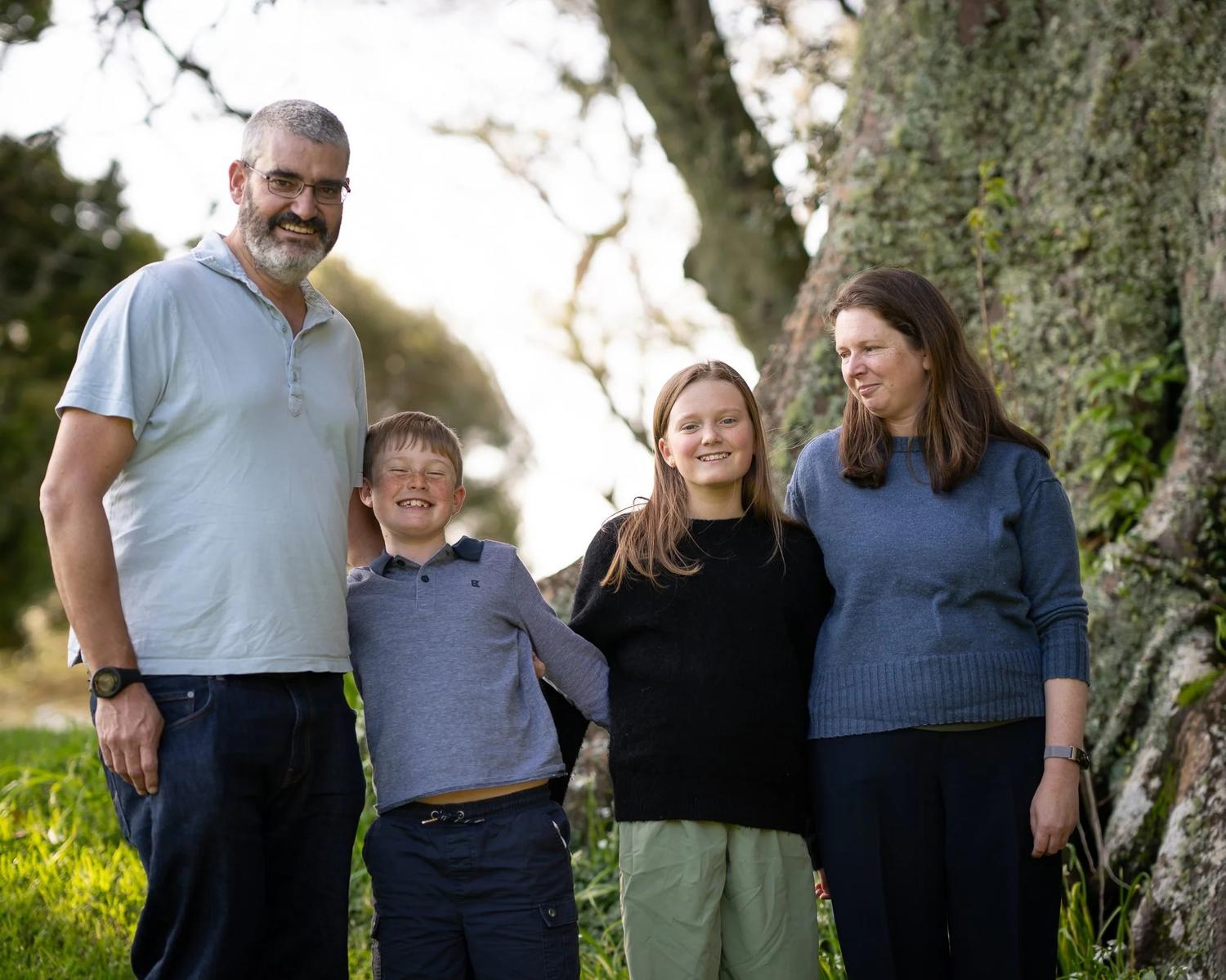 The family stands together beneath a large old tree