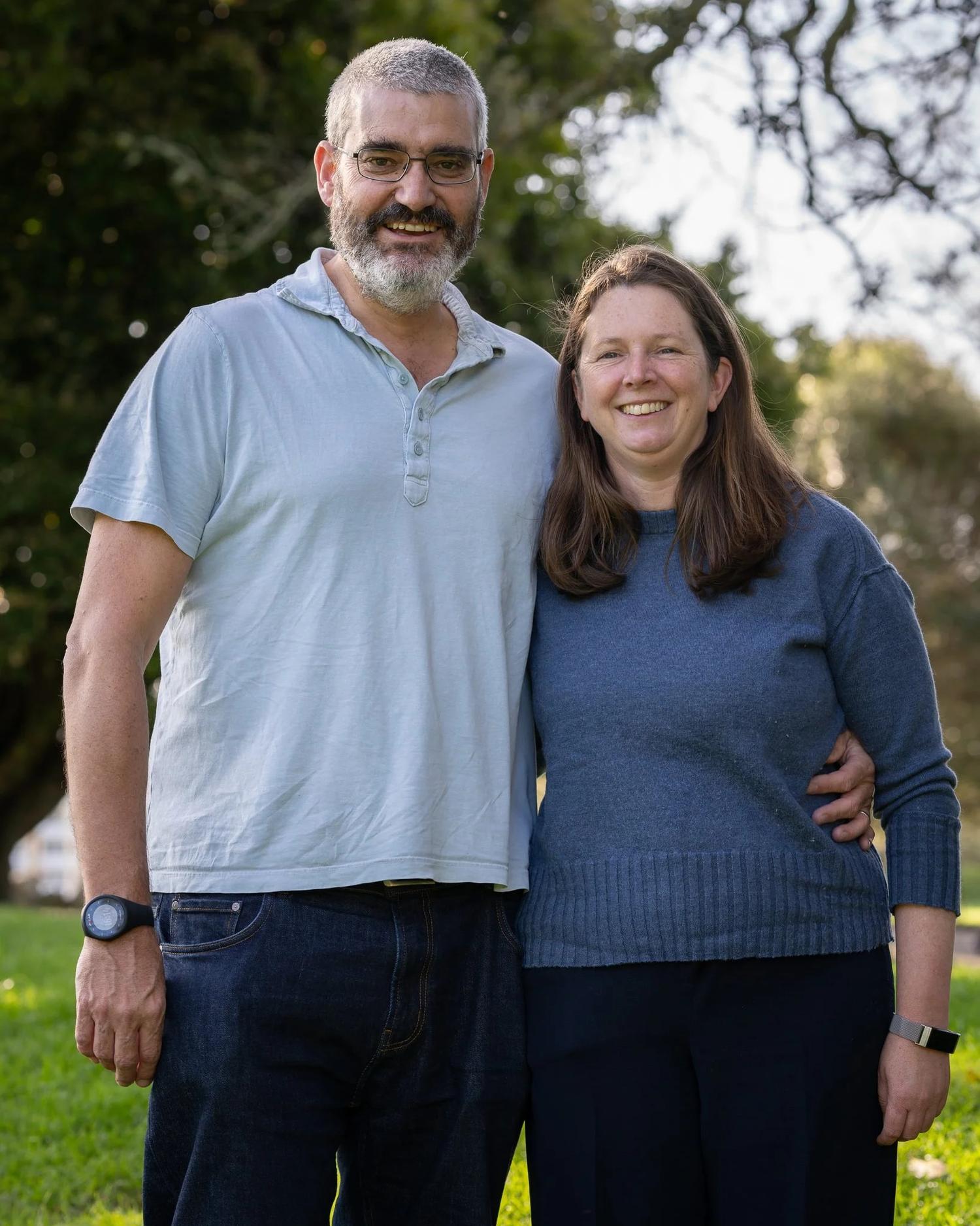 The parents stand arm in arm in the park