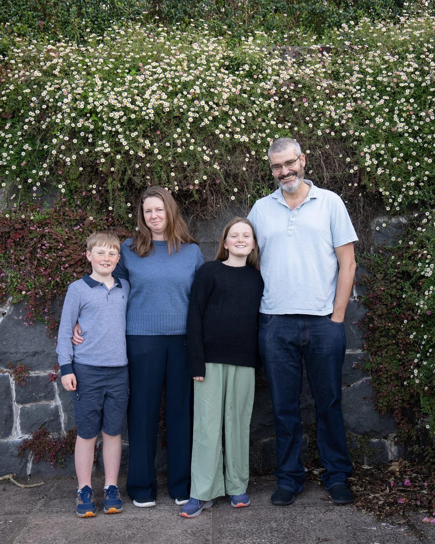 The family in front of a stone wall covered in white flowers
