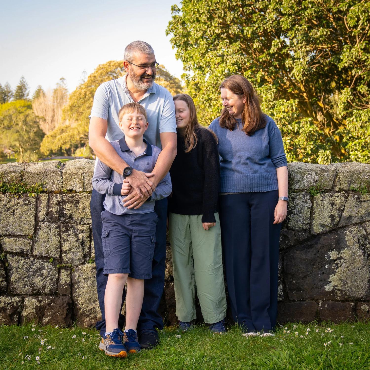 The family stands in front of a stone wall in golden light
