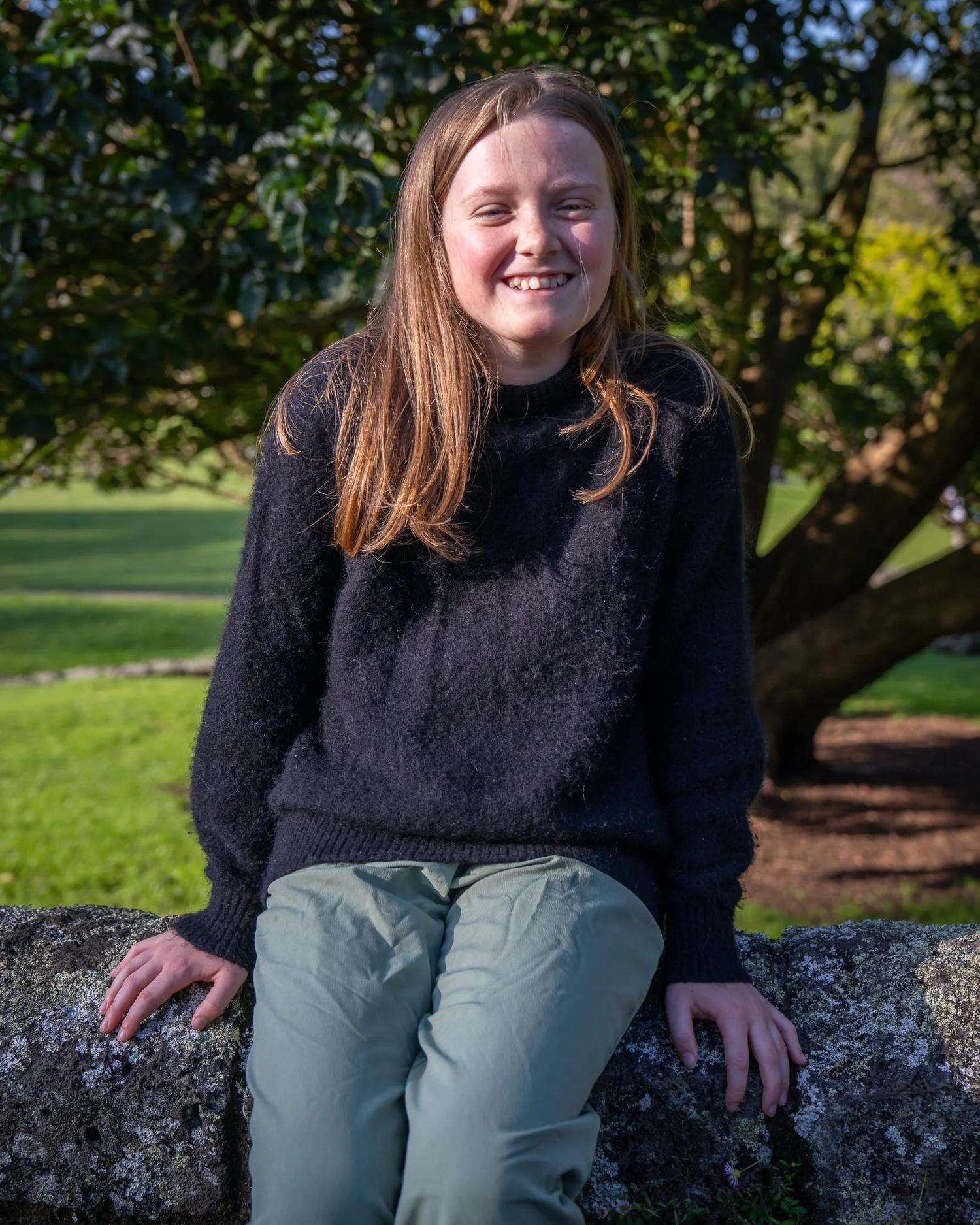 A girl sits on a rock smiling at the camera