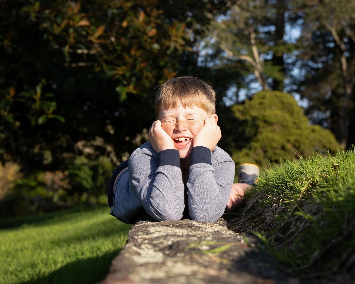 A boy lies on a stone wall resting his chin in his hands