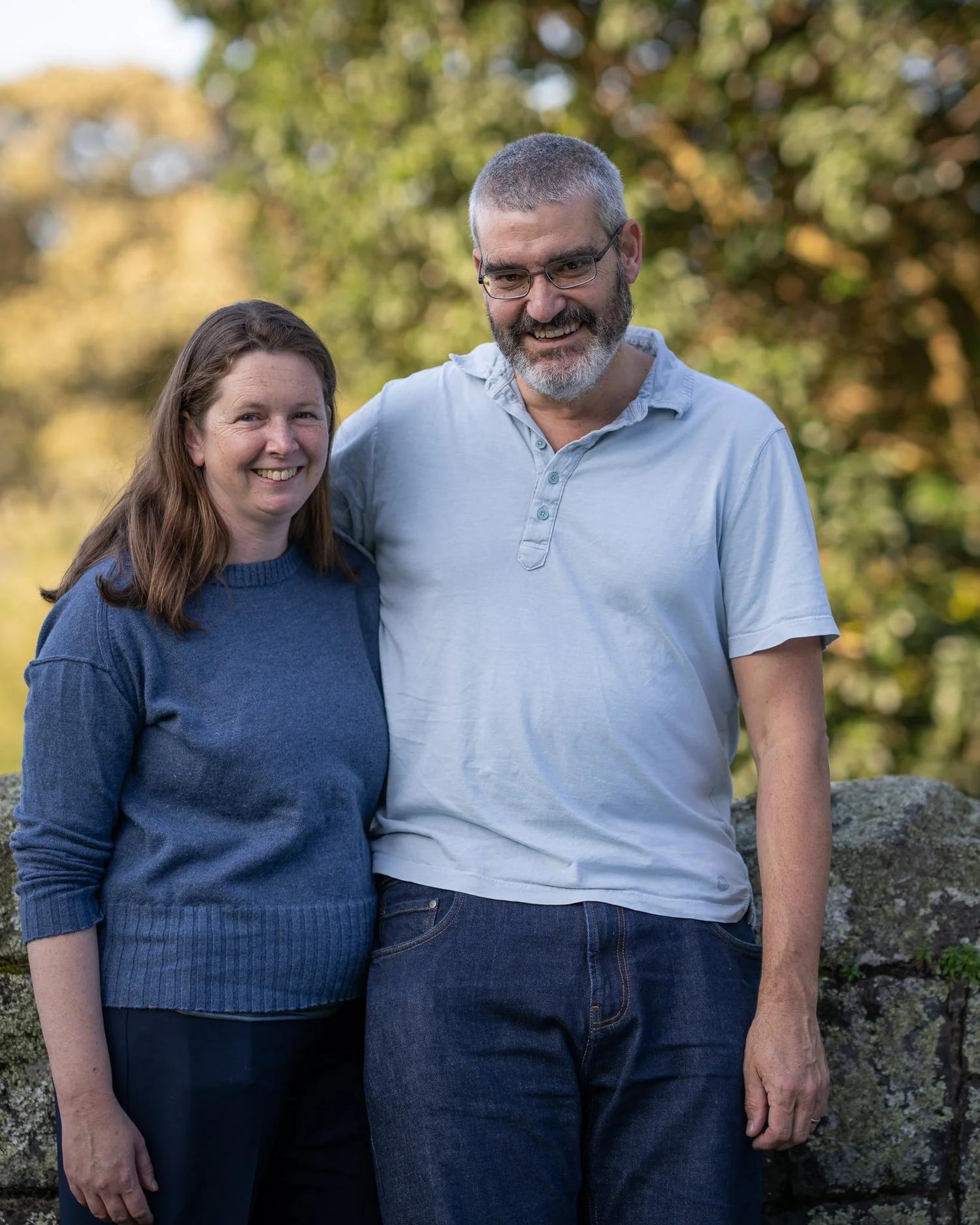 The parents stand together in front of a stone wall