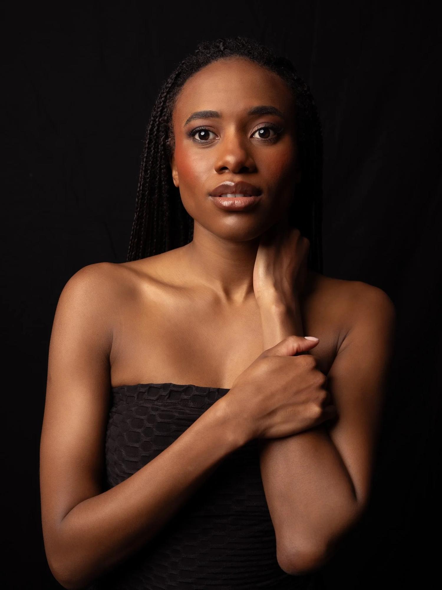 Ty with her hand at her neck against black