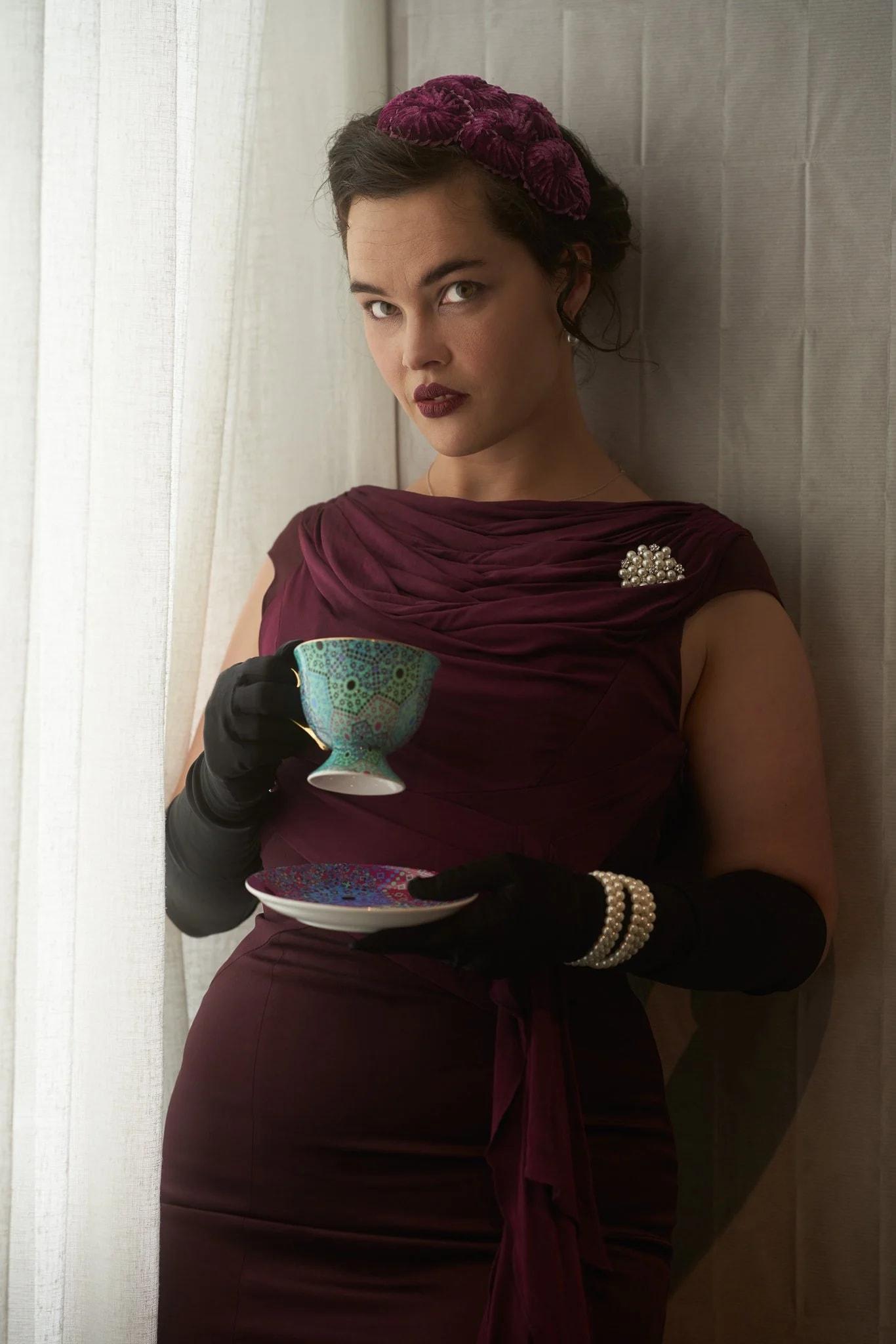 Anita holds a teacup by a sheer curtain