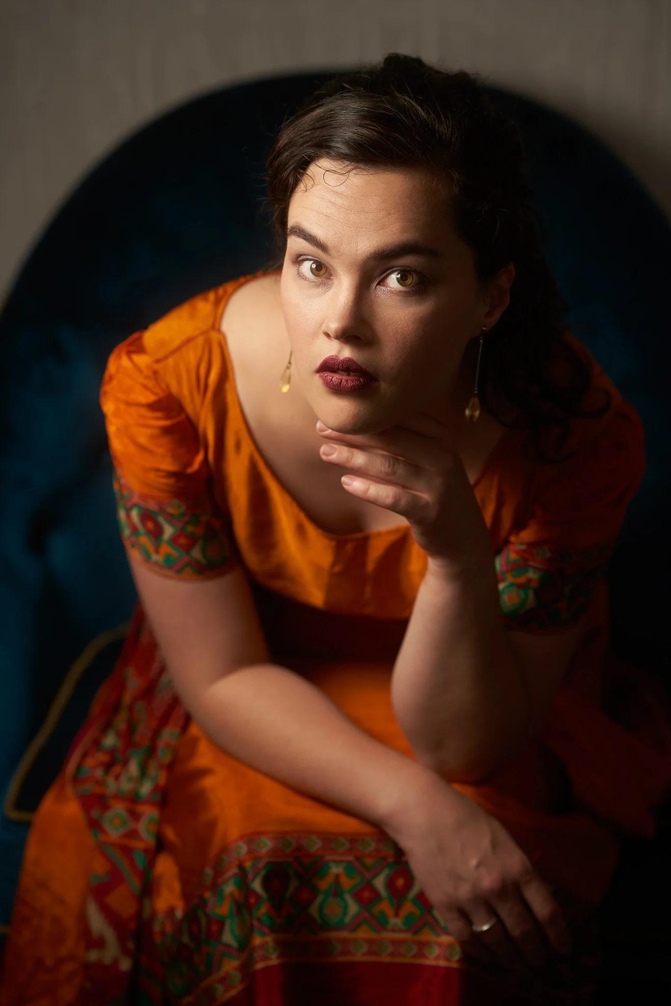 Anita leans forward in an orange dress