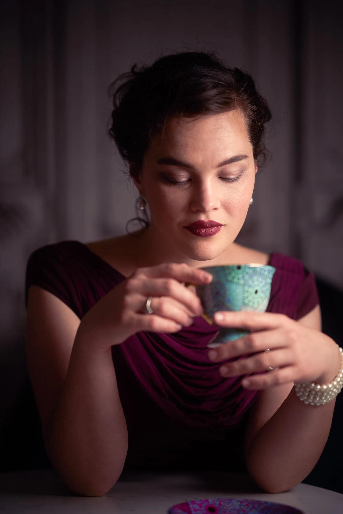 Anita cradles a turquoise teacup in a burgundy dress