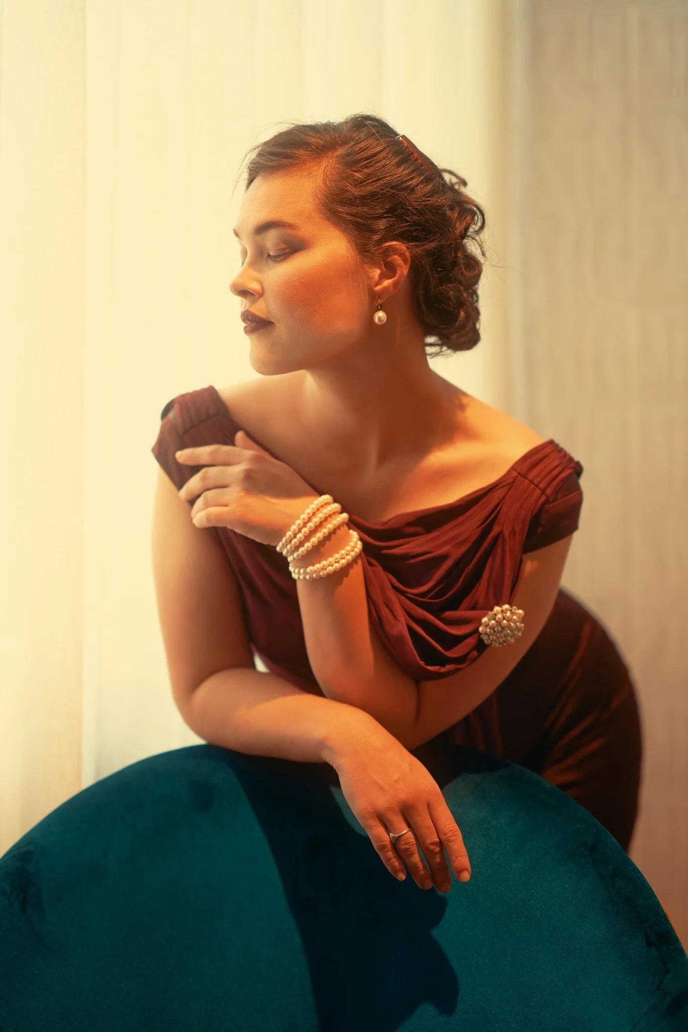 Anita in a burgundy dress leaning on a teal velvet chair at the Fable