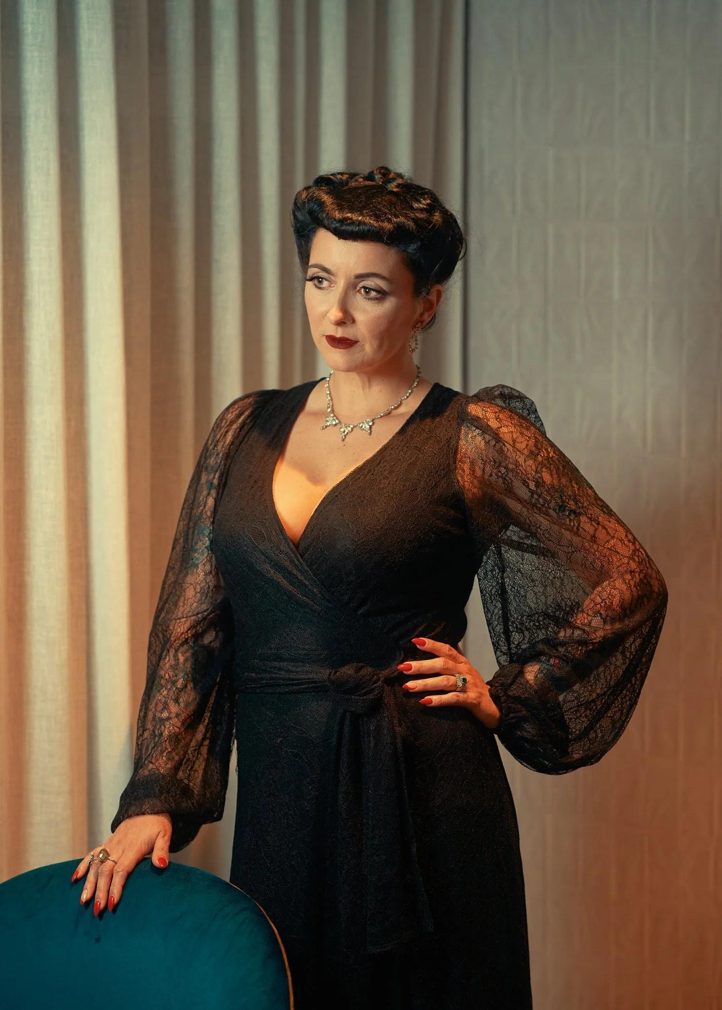 Viv in a black lace gown with a hand on her hip