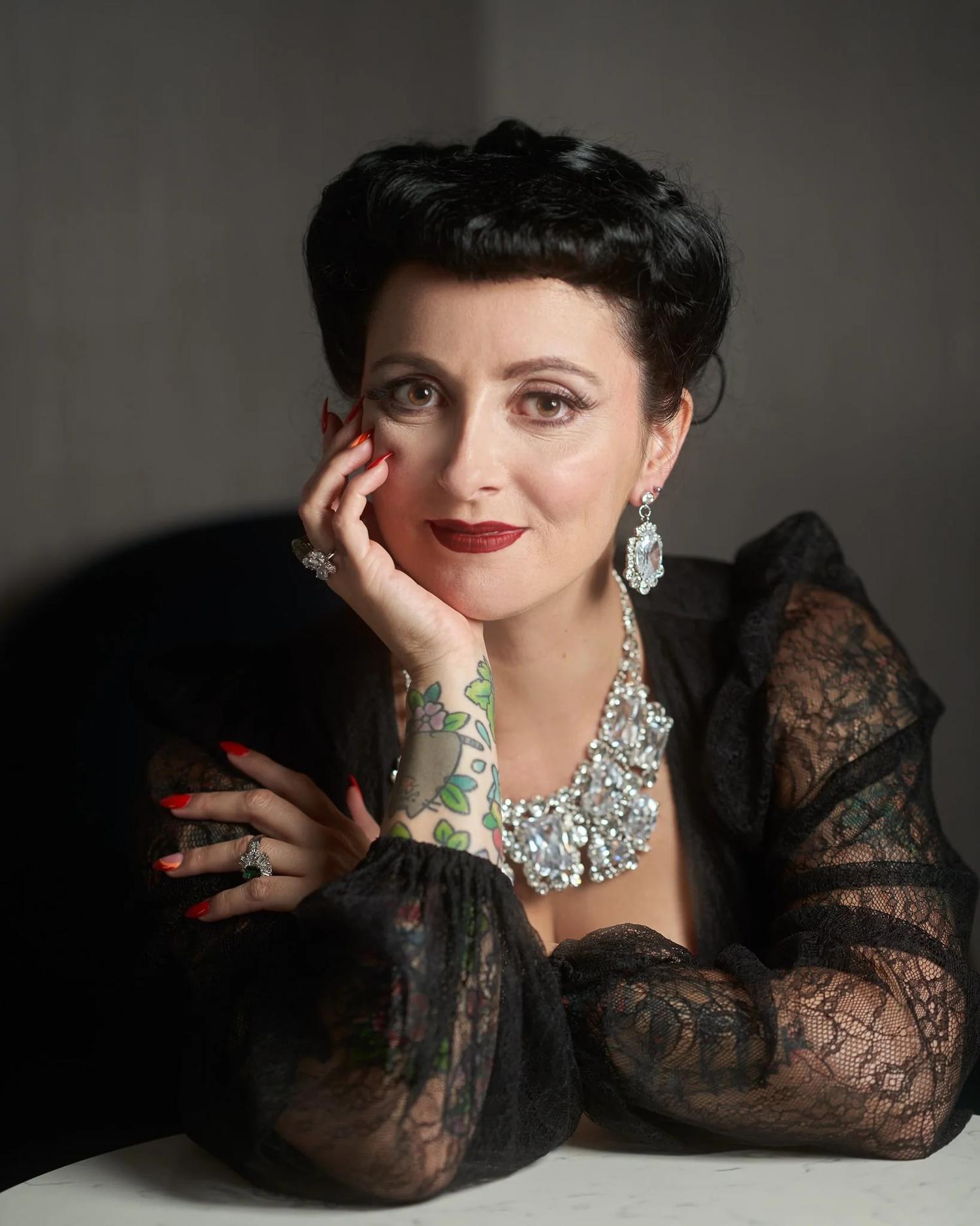 Viv smiles with her chin on her hand in sparkling jewellery