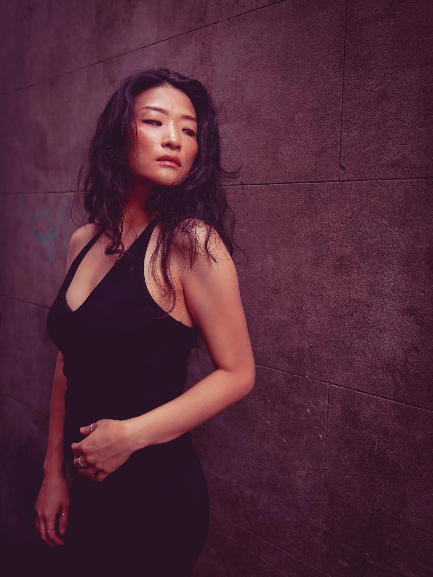 Anna in a black halter top against a purple-toned wall
