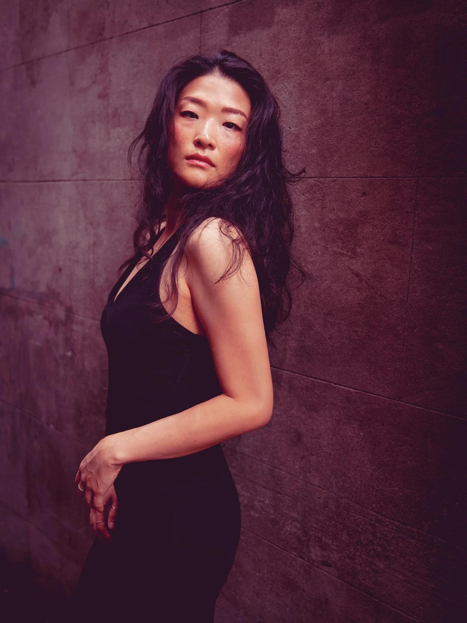 Anna glances over her shoulder against a dark textured wall