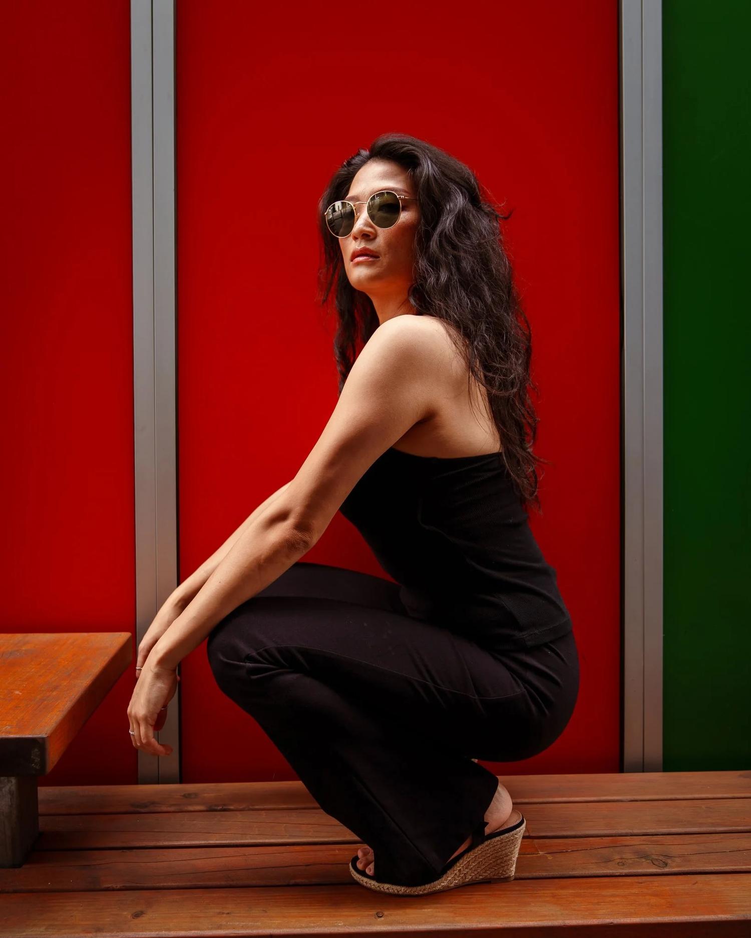 Anna in sunglasses crouching on a bench beside a red door