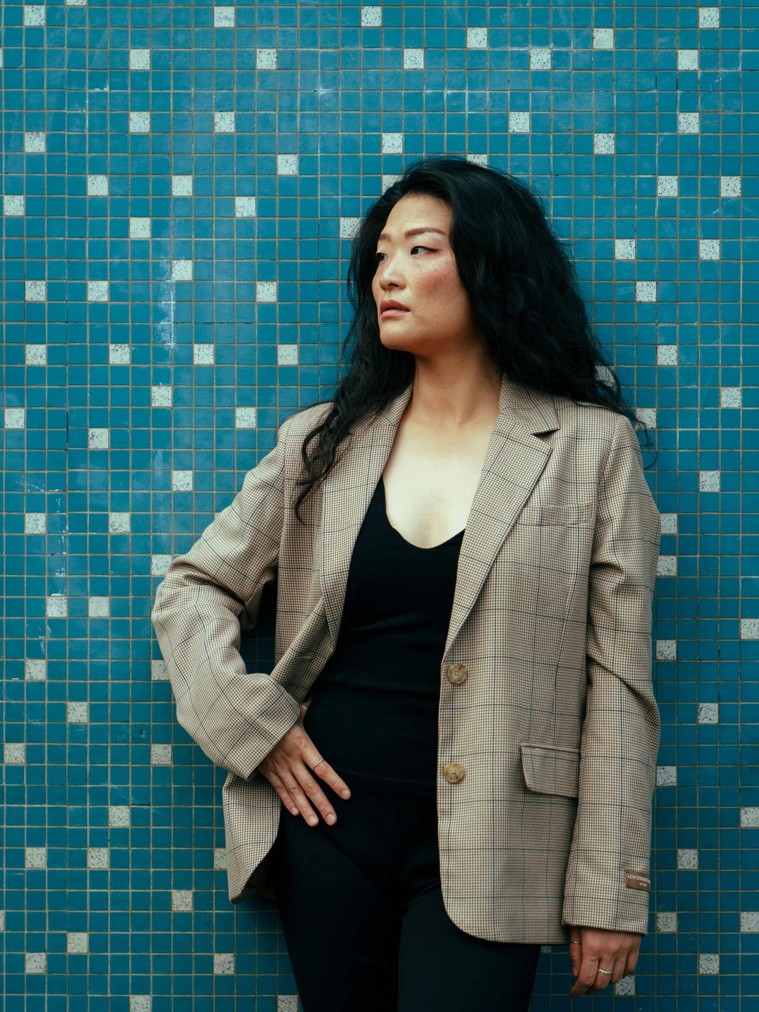 Anna in a checked blazer against a blue mosaic tile wall