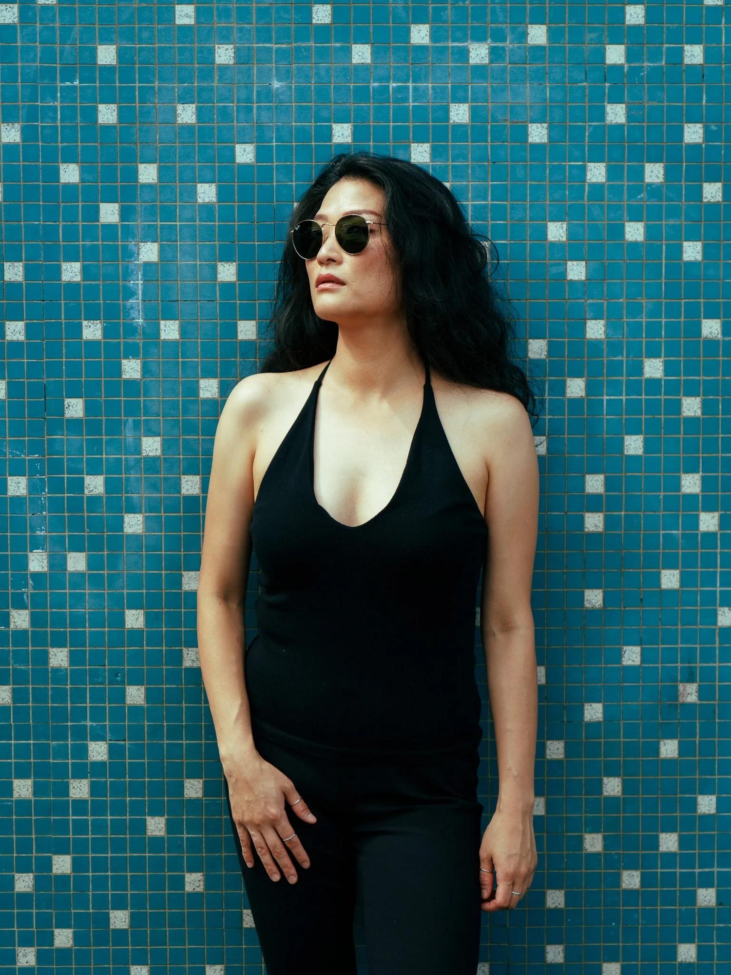 Anna in sunglasses and a black halter top against blue tiles