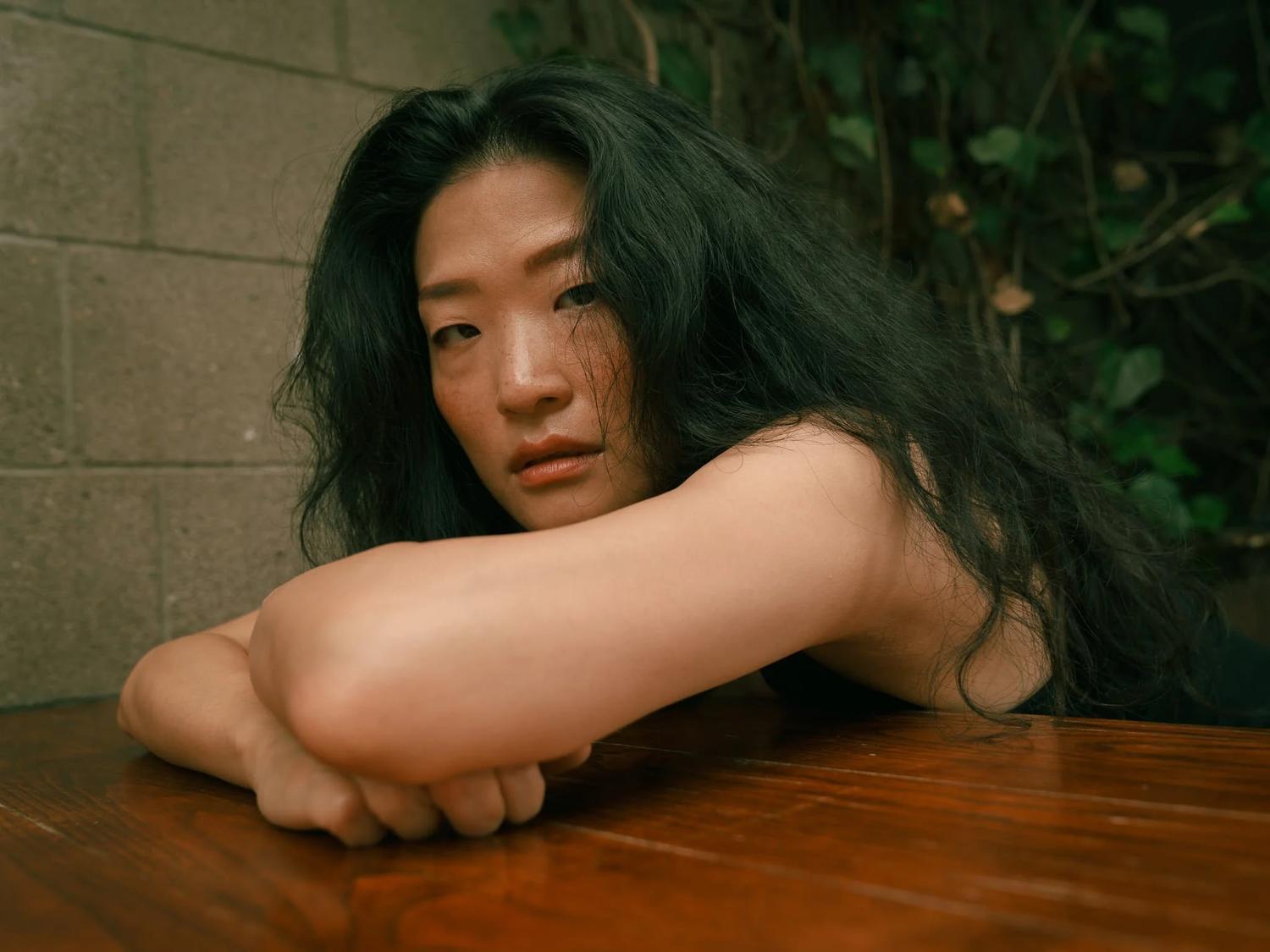 Anna rests her arms on a wooden table looking at the camera