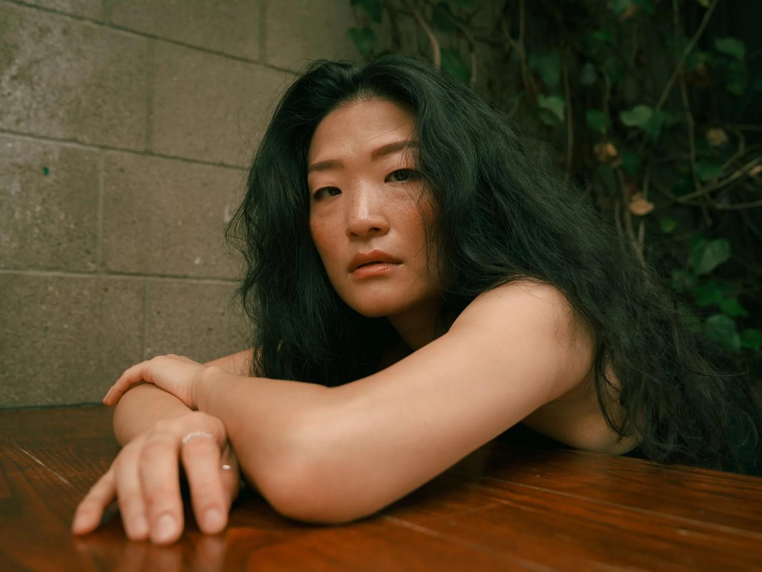 Anna leans on a table in front of an ivy-covered wall