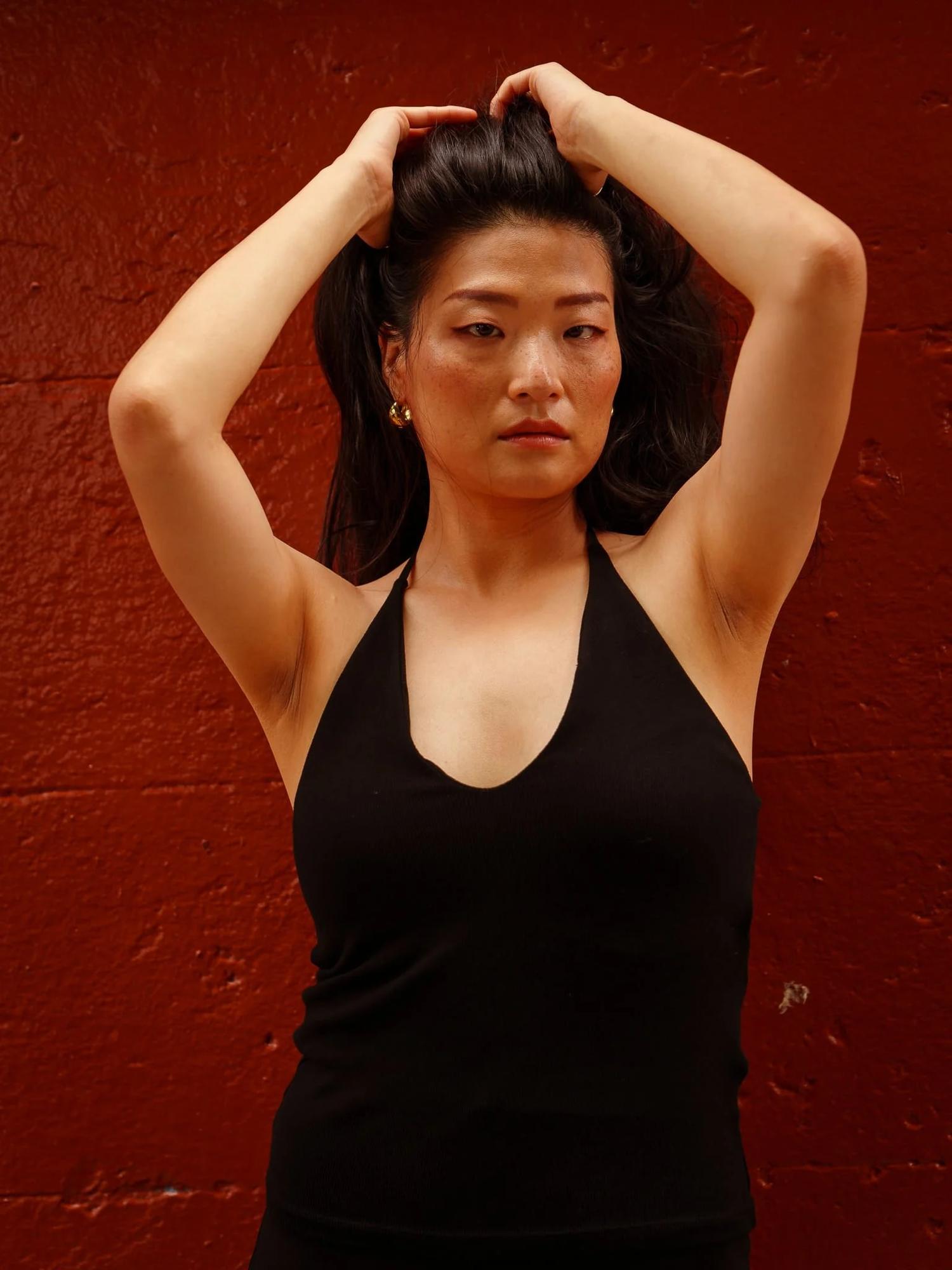 Anna with both hands in her hair in front of a red wall