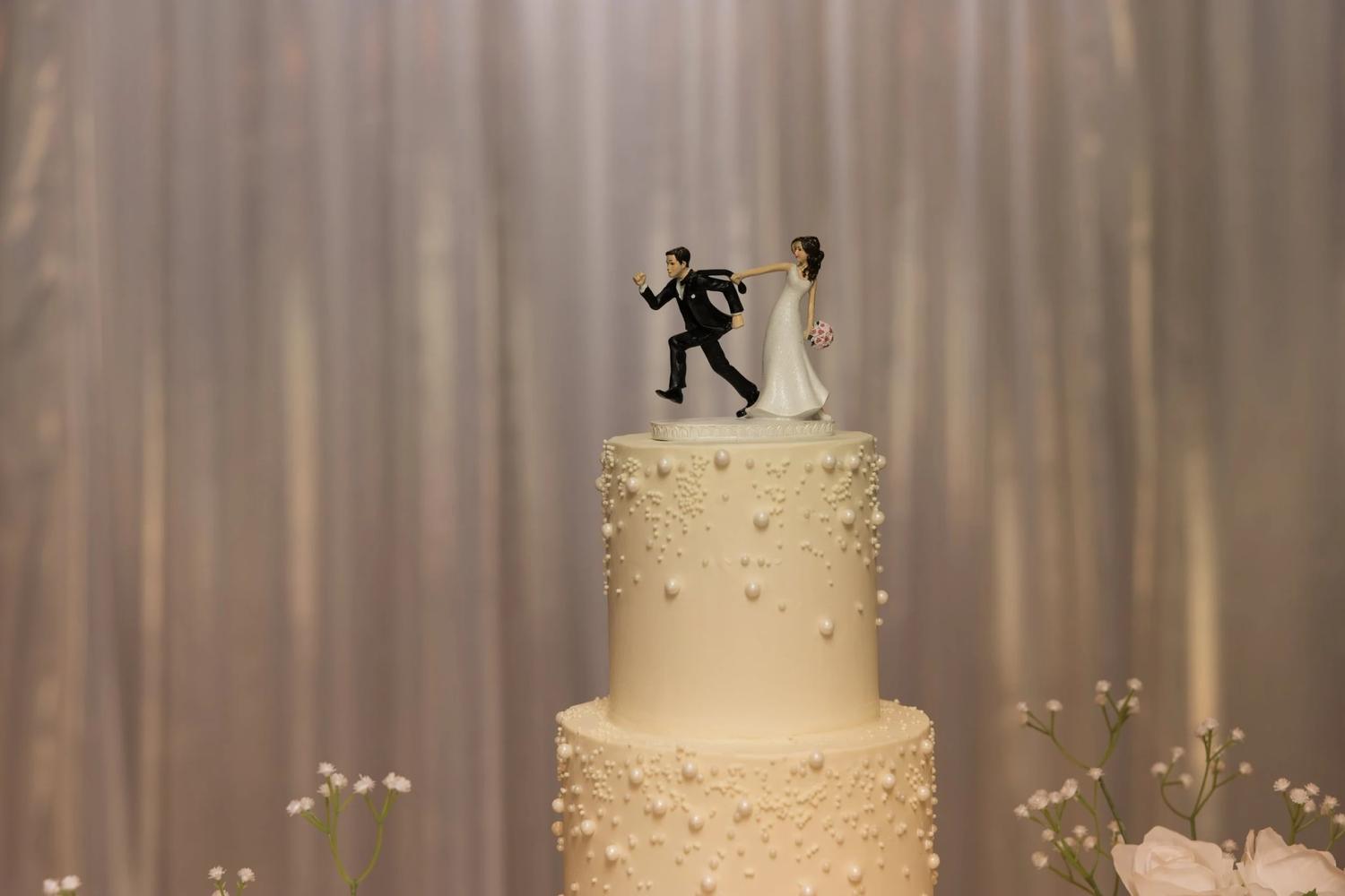 Two-tier white wedding cake with a running bride and groom cake topper