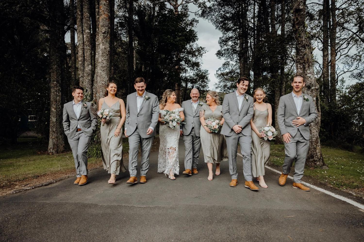 Wedding party in grey suits and sage dresses walking through a forest