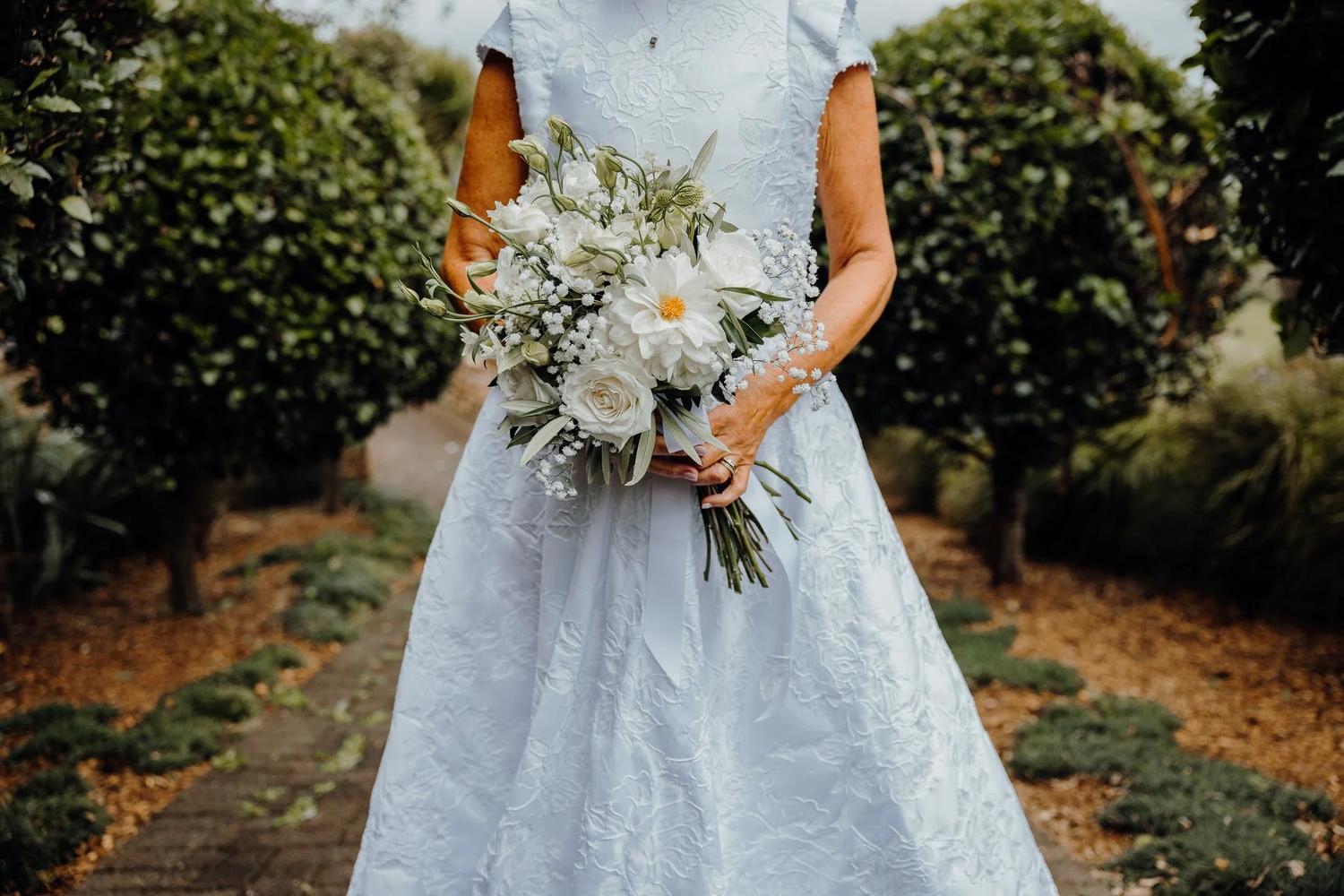 Bride holding a white bouquet of roses and daisies in a garden