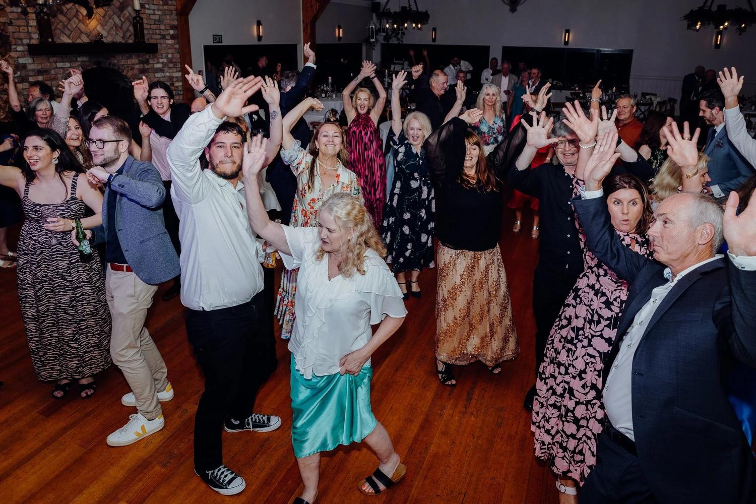 Wedding guests dancing with their hands in the air on a packed dance floor