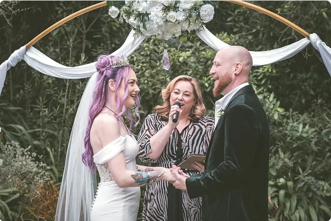 Celebrant Anna leading a garden ceremony as the couple hold hands under a floral arch