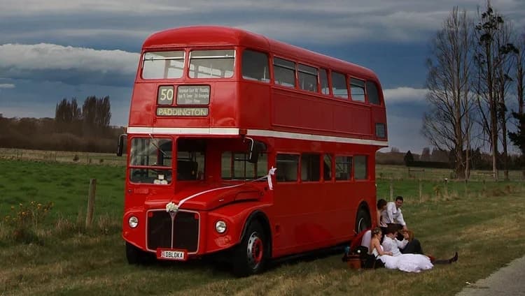 Wedding party relaxing on the grass beside a red London Routemaster double-decker bus
