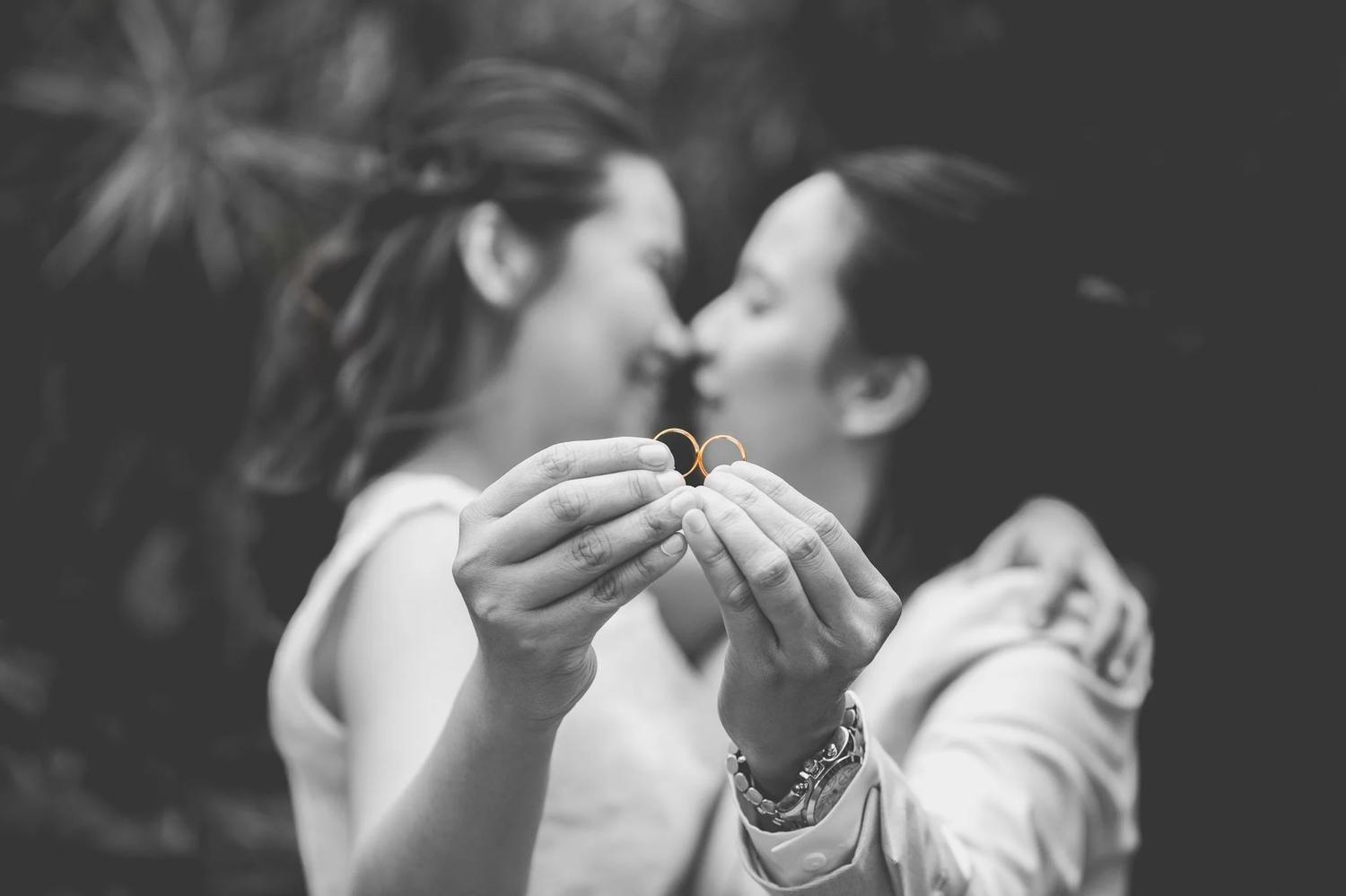 Black and white photo of a couple kissing as they hold up their wedding rings
