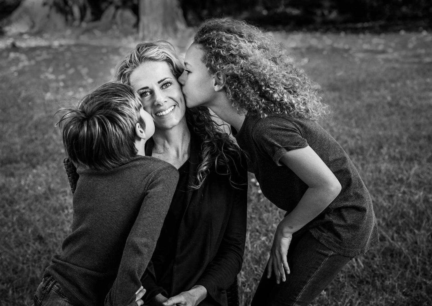 Black and white photo of children kissing their mother's cheeks