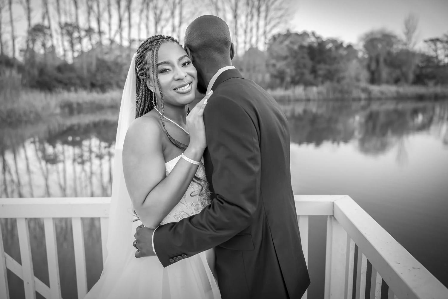 Black and white photo of a bride and groom embracing on the deck by the lake at Abel Estate