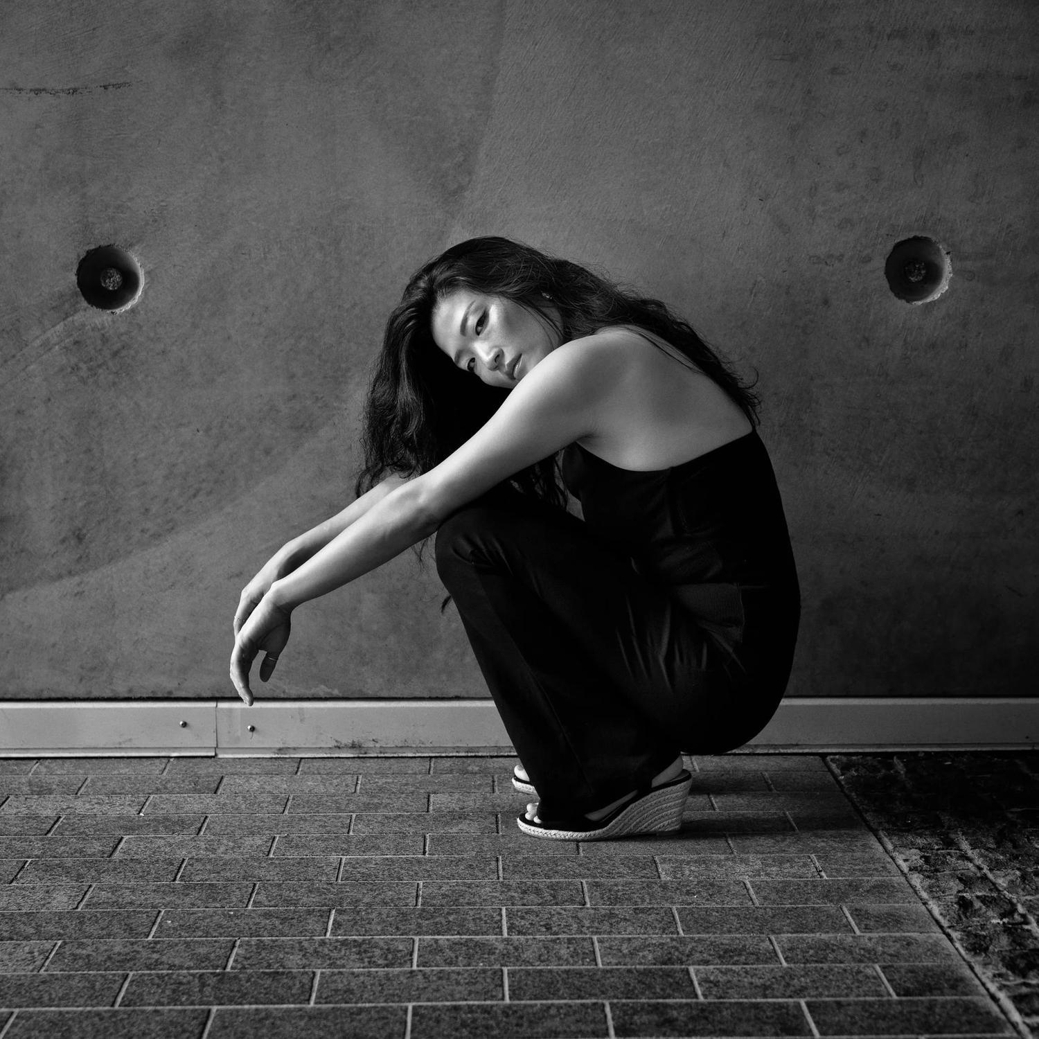 Black and white photo of Anna crouching against a concrete wall