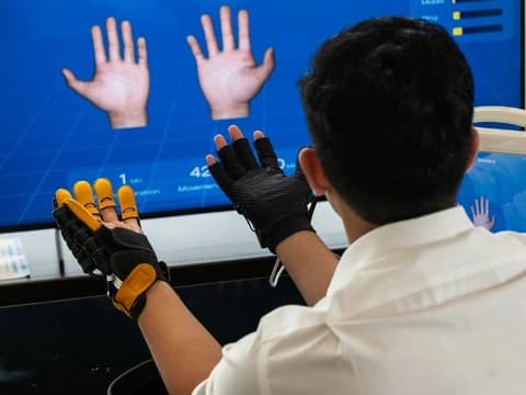 ผู้รับบริการฝึกมือด้วยถุงมือหุ่นยนต์แบบสองข้างหน้าจอแสดงผล