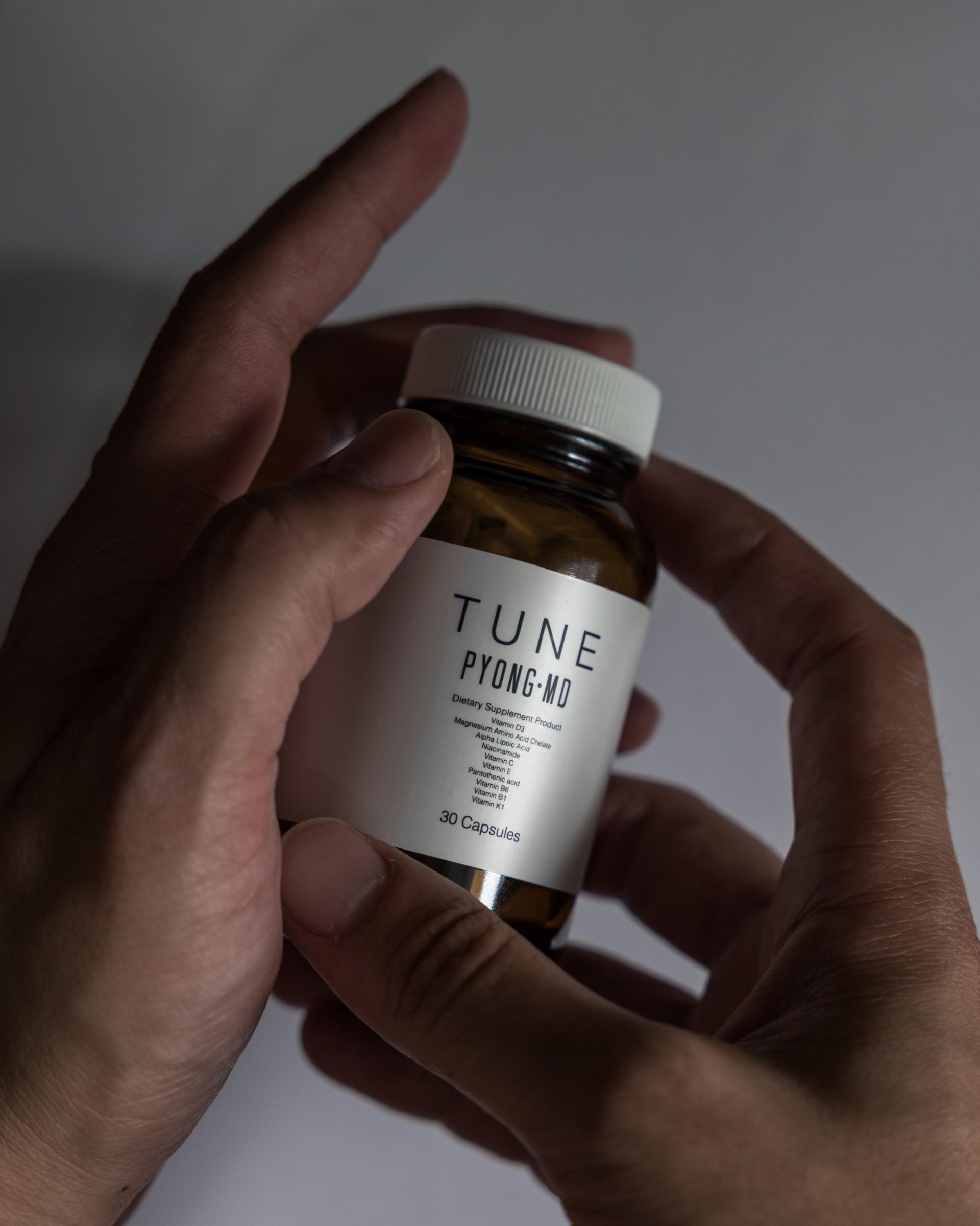 สองมือถือขวด TUNE PYONG MD สีชาบนพื้นหลังสีเข้ม