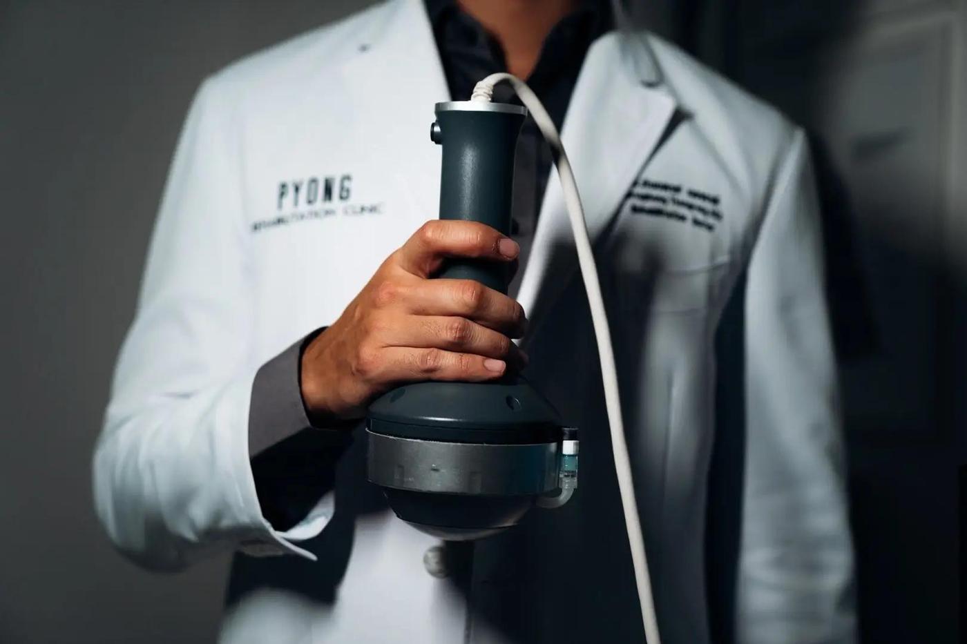 طبيب يحمل رأس جهاز الموجات التصادمية المركزة في عيادة PYONG Rehabilitation