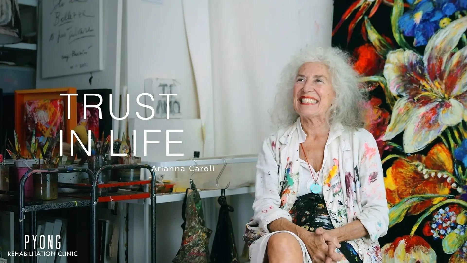 Arianna นั่งยิ้มในสตูดิโอศิลปะข้างภาพวาด พร้อมข้อความ Trust in Life