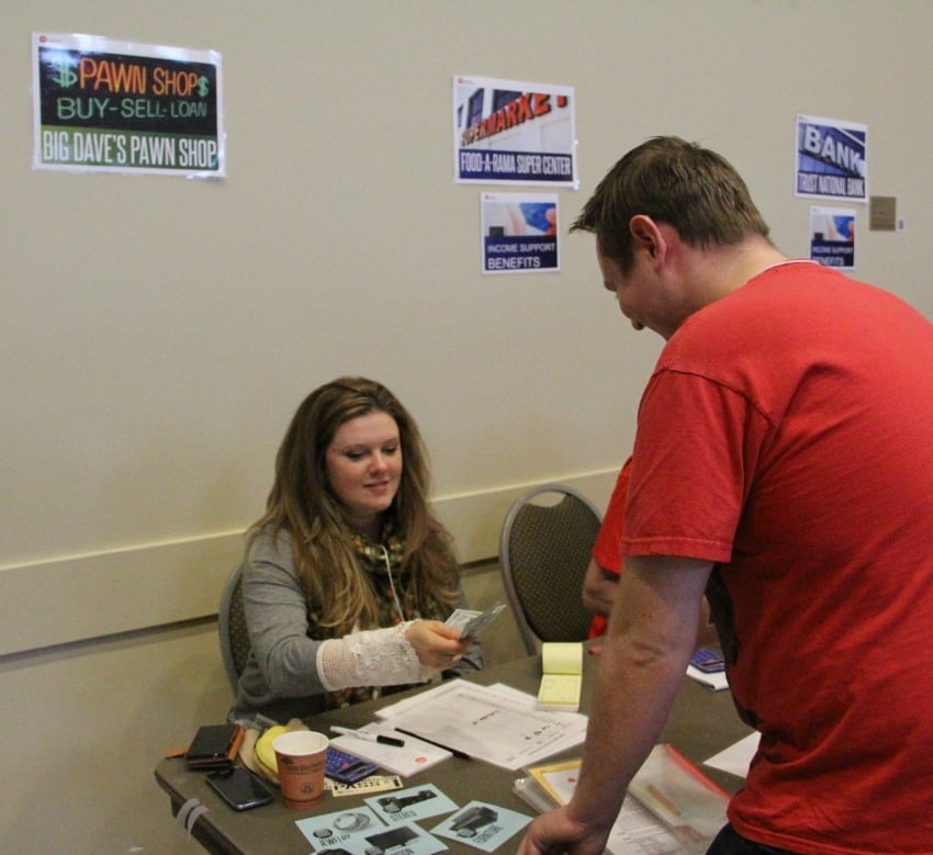 <who> Photo Credit: KelownaNow. </who> Participants had to go around to different booths to earn money, like the pawn shop, and quick cash centre. 