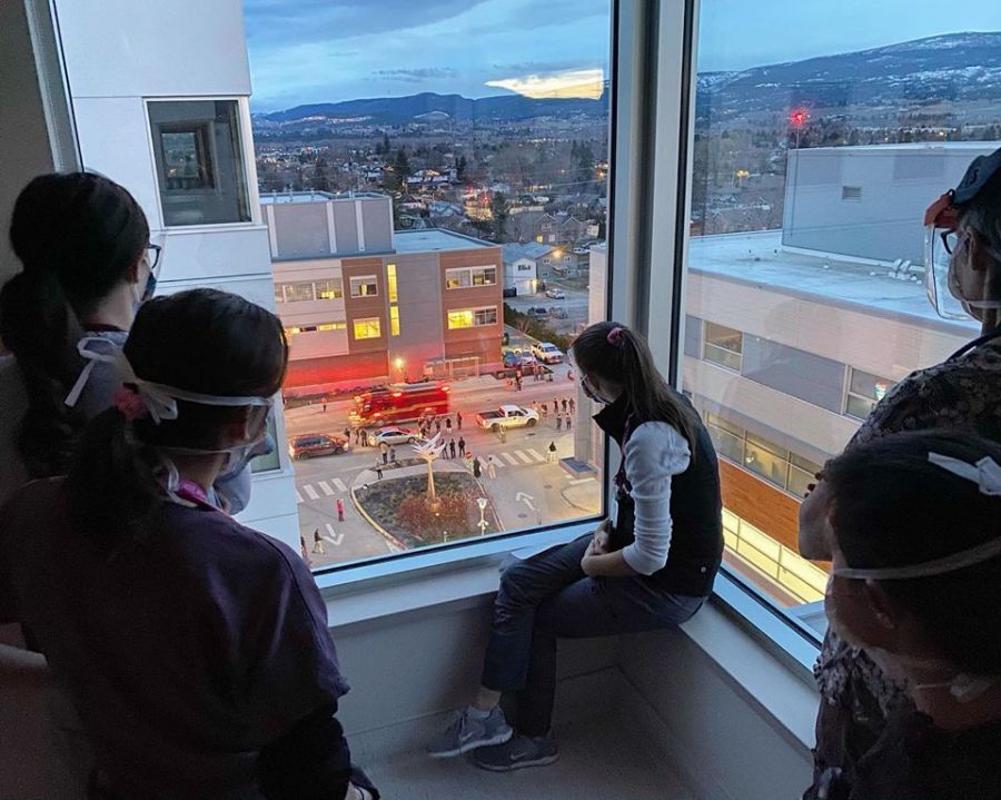 <who>Photo Credit: Amy Martens</who>Nurses inside Kelowna General Hospital's COVID-19 unit take a moment to watch Saturday night's procession of emergency vehicles in front of the hospital.