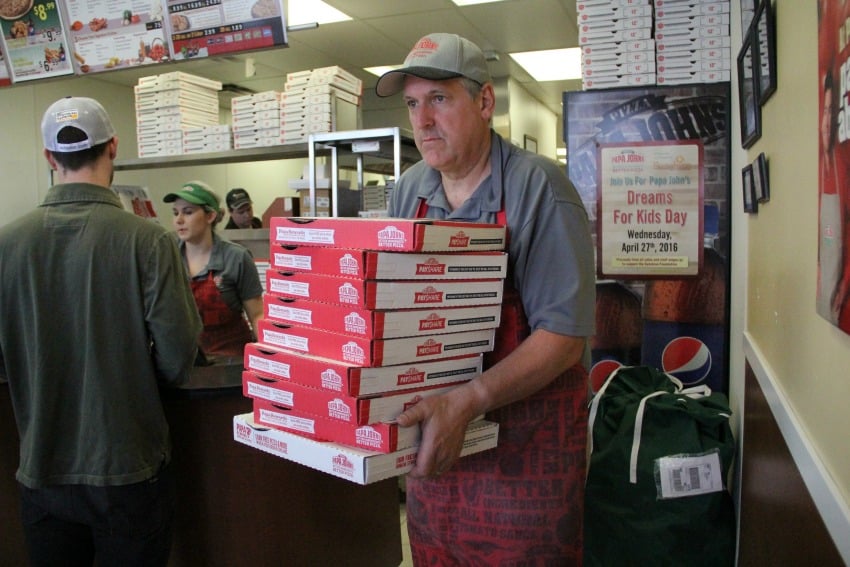 <who> Photo Credit: KelownaNow. </who> Papa John's B.C. Director of Operations Scott Patten carrying out pizzas for a supporter. 