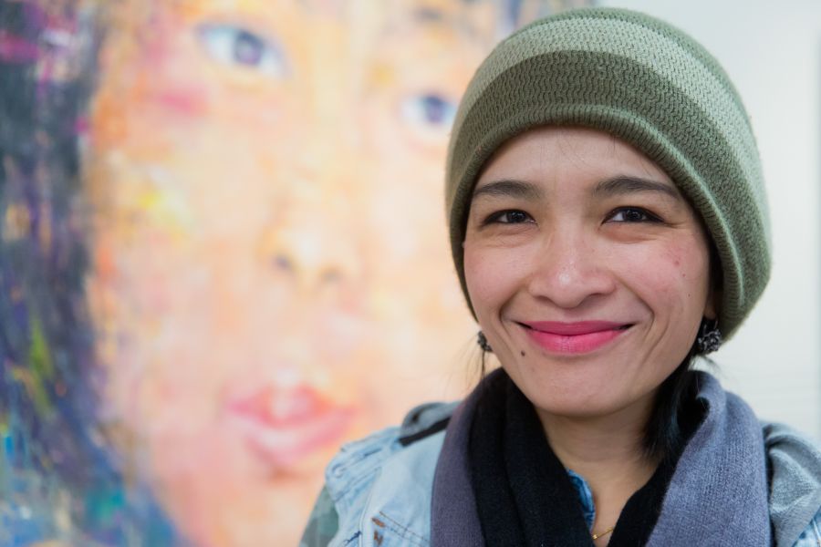 <who> Photo credit: NowMedia </who> Nalidsa Sukprasert, with one of her two paintings at the exhibit in the background.