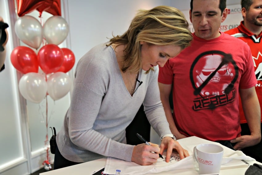 <who> Photo Credit: KelownaNow.com </who> Hayley Wickenheiser signs an autograph for a QHR Technologies staff member.