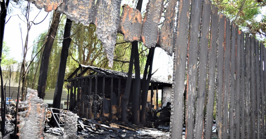<who> Photo Credit: KelownaNow/Steve MacNaull </who> A shot through the scorched fence to the destroyed shed.