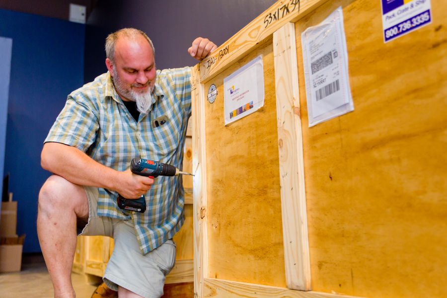<who>Photo credit: NowMedia</who> Gallery curator Paul Crawford opens the first crate of Bob Ross paintings Thursday afternoon.