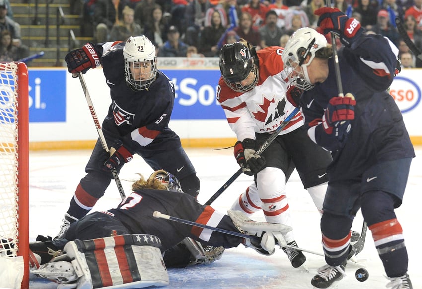 <who>Photo Credit: Lorne White/KelownaNow.com </who>Laura Fortino of Canada tries to find the puck while United States goalie Alex Rigby reaches to corral it.